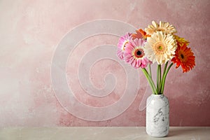 Bouquet of beautiful bright gerbera flowers in vase on marble table against color background.