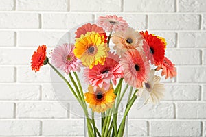 Bouquet of beautiful colorful gerbera flowers in vase against white brick wall