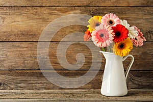 Bouquet of beautiful colorful gerbera flowers in vase on wooden table. Space for text