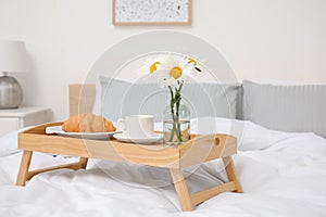 Bouquet of beautiful daisy flowers and breakfast on wooden tray in bedroom