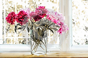 Bouquet of beautiful fresh bright pink peonies in glass transparent vase on background of window. Retro toned image