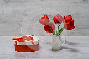 Bouquet of beautiful fresh red tulips in small white jug and gift box in heart shape on light background. Valentine`s, women`s o
