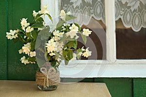 Bouquet of beautiful jasmine flowers in vase on wooden table near window outdoors, space for text