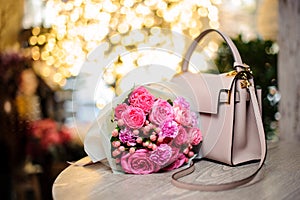 Bouquet of beautiful pink flowers near the stylish handbag on the table