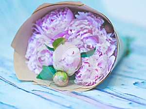 A bouquet of beautiful pink peonies on a bluish wooden table against soft-focused background.