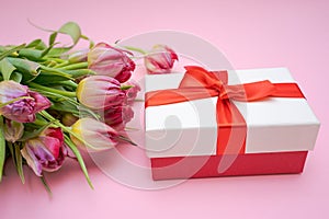 Bouquet beautiful pink tulips lies with gift box with red ribbon. Light pink