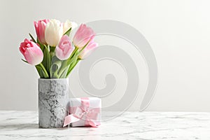 Bouquet of beautiful spring tulips in vase and gift box on marble table against light background.