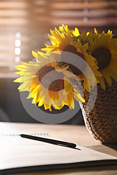 Bouquet of beautiful sunflowers, notebook and pencil  on table indoors, closeup
