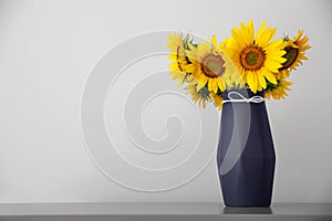 Bouquet of beautiful sunflowers in vase on table near light wall. Space for text