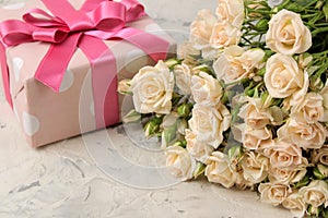 A bouquet of beautiful tender mini roses and a gift box on a light concrete background. holidays. presents