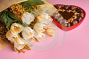 Bouquet with beautiful tulips, mimosa flowers and box of chocolate candies in shape of heart on pink background