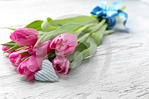 Bouquet of beautiful tulips and small cotton heart on light wooden background