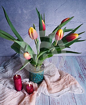 Bouquet of beautiful yellow-red tulips in a leafy vase and red candles.