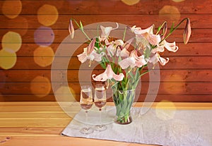 Bouquet of beige colored lilies with pink spots in glass  vase and two glasses of champagne.