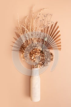 Bouquet of beige dried flowers, grass and leaves in a glass vase on beige background top view