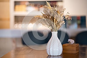 Bouquet of beige dried flowers in white vase on table against morning light background