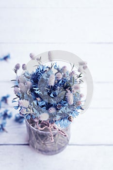 Bouquet of blue cornflowers flowers in a glass jar on an old white wooden board. Floral vintage background with wildflowers