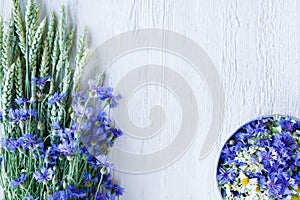 Bouquet of blue flowers cornflowers with ears of wheat and flower buds in a round plate on an old white wooden board.