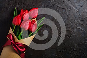 Bouquet with bow-knot ribbon of red tulip flowers on textured black background