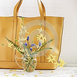 Bouquet of bright colorful flowers in glass vase on the background yellow handbag close-up. Concept of spring or summer