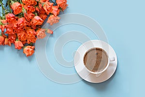 Bouquet of bush orange roses and cup of black coffee on pastel blue background. Flat lay. Copy space.