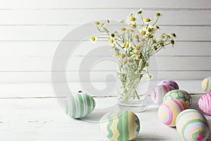 Bouquet of chamomiles in a glass vase and easter eggs in pastel color on white wooden table