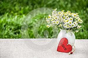 Bouquet of chamomiles and red heart. summer flowers on table in the garden. Natural garden background.