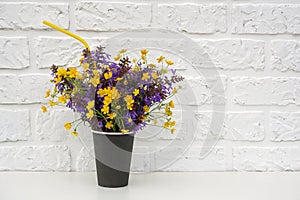 Bouquet of colored flowers in black paper coffee cup with cocktail straw on background white brick wall, Copy space Mockup