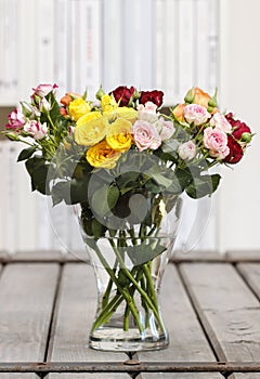 Bouquet of colorful roses in glass vase on vintage wooden table