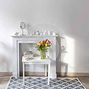 Bouquet of colorful tulips in a glass figured vase on a white fireplace console. A faience figurine of angel as an interior photo