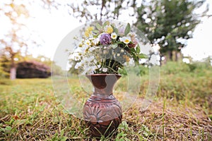 Bouquet of colorful wild wild flowers in a broken clay pot laid on the grass