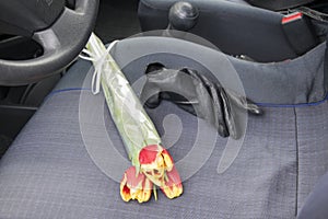 The bouquet consists of three red-yellow tulips. Flowers are on the seat in the car`s interior.