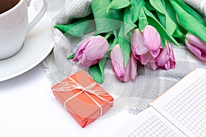 Bouquet of cut pink lilac tulips with a red gift box and a cup of black coffee on white background close up
