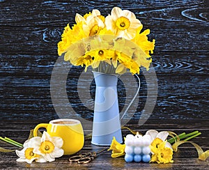 A bouquet of daffodil flowers in a blue vase, a yellow cup of coffee, a blue candle on a dark wooden backgroundGenerated image