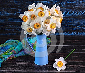 Bouquet of daffodils flowers in blue vase, colorful shawl on dark wooden background. Generated image