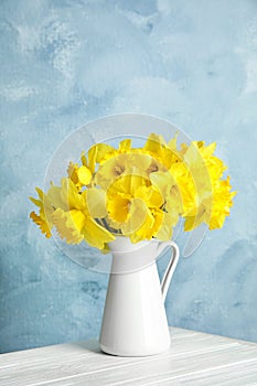 Bouquet of daffodils in jug on table against color background, space for text.