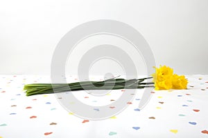 a bouquet of daffodils placed on a tablecloth patterned with multiple colored hearts