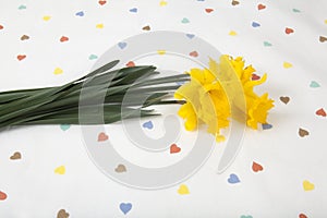 a bouquet of daffodils placed on a tablecloth patterned with multiple colored hearts