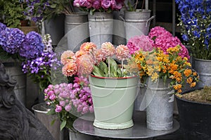 Bouquet of dahlias in a galvanized bucket stands on a chair near the entrance to the store.