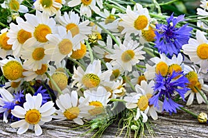 A bouquet of daisies and cornflowers on wooden table.
