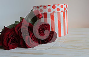 A bouquet of red roses is on the table with a gift box.