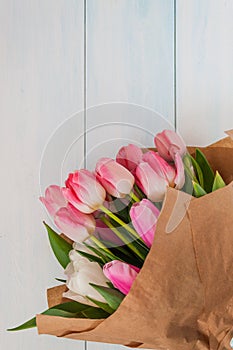 Bouquet of delicate pink tulips in craft paper on a light wooden background.