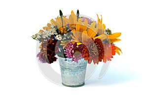 A bouquet of different flowers stands in a small decorative bucket on a white background