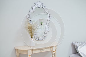 A bouquet of dry wildflowers stands in a white vase on a boudoir table by a vintage mirror