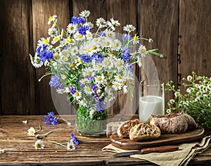 Bouquet of field flowers, glass of milk and soft bread.