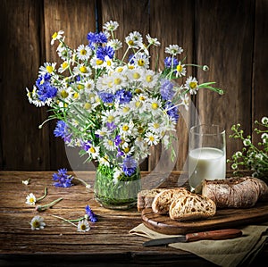 Bouquet of field flowers, glass of milk and soft bread.
