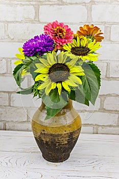 Bouquet of flowers in antique rustic clay jug against white brick wall