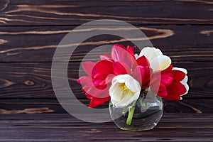 Bouquet of flowers on dark wooden boards background, romantic frame, holiday gift card. Red and white tulips in glass vase, still