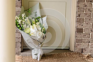 A bouquet of flowers delivered on a porch doorsteps of a house front door. Surprise contactless delivery. Mother`s Day, Valentine
