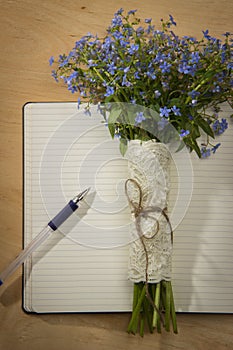 A bouquet of flowers forget-me, notebook and pen on the wooden t